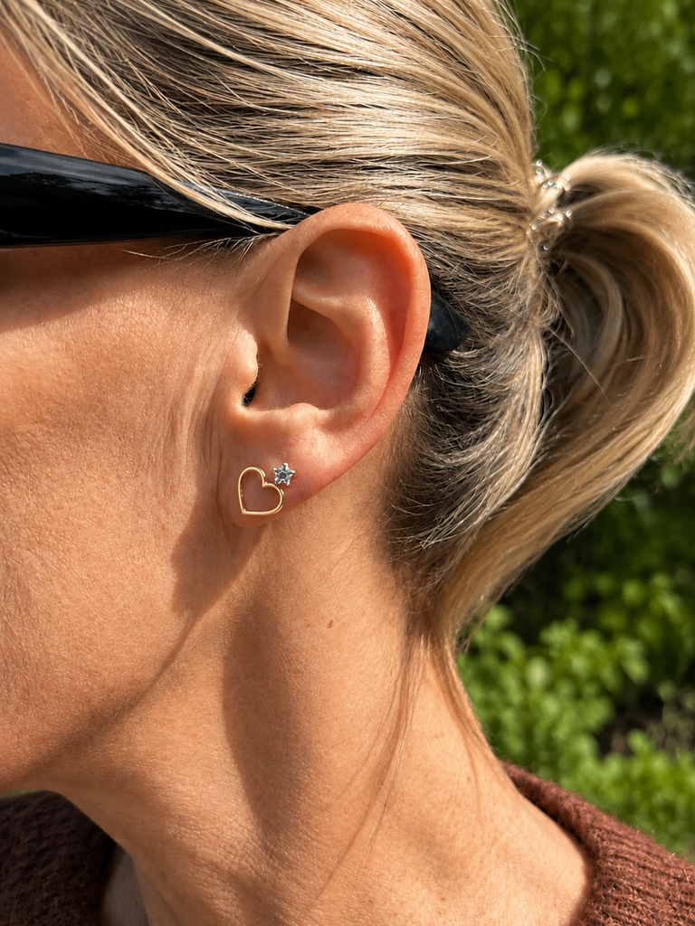 Close-up of a person wearing a heart-shaped earring with a green outdoor background