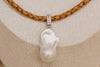 Pearl pendant with diamond accents on a braided leather cord against a beige fabric background