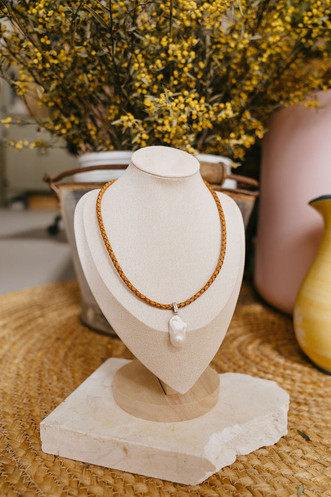 Necklace with a pendant on a beige bust in front of yellow flowers