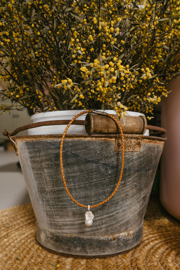 Necklace with a pendant on a rustic metal bucket with yellow flowers in the background