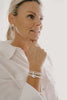 Woman wearing a white shirt and pearl bracelet on a plain background
