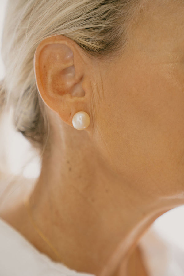 Close-up of a pearl earring on an ear with a blurred background
