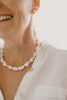 Close-up of a person wearing a pearl necklace and earrings on a blurred background