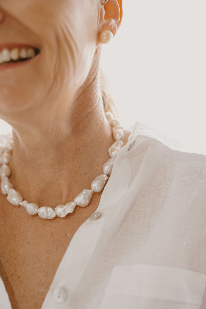 Close-up of a person wearing a pearl necklace and earrings on a blurred background