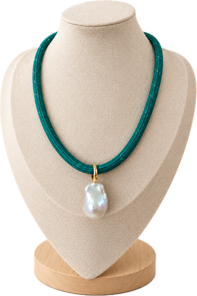A teal green braided cord necklace with a large, irregular white baroque pearl pendant and a small gold clasp, displayed on a beige fabric jewelry bust.