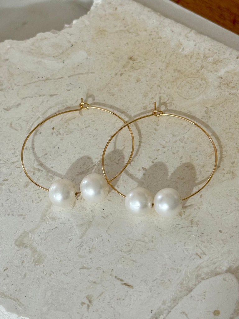 Gold hoop earrings with pearls on a textured stone surface