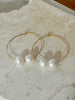 Gold hoop earrings with pearls on a textured stone surface