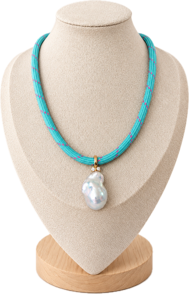 A turquoise beaded necklace with a large white baroque pearl pendant, displayed on a beige fabric jewelry bust against a white background.