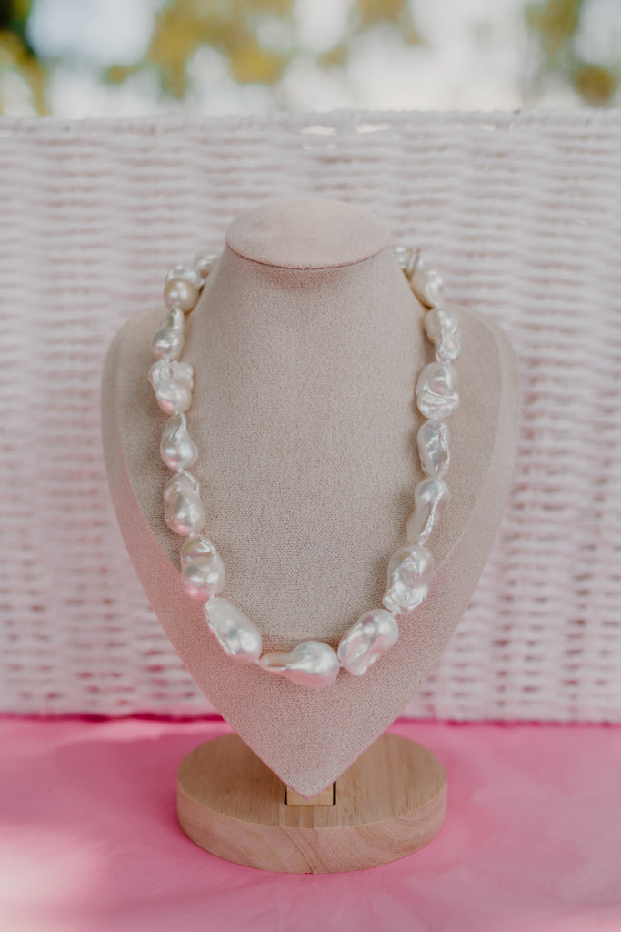 Pearl necklace on a mannequin bust with a pink background
